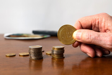 Stacks of coins on the table and Bitcoin in the hands of a man. Close up.