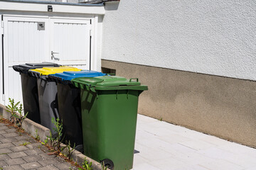 Multi-colored plastic bins for separate waste collection standing in a row near the garage.