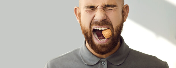 Studio head shot of young man with strong and sturdy teeth trying to crack walnut. Close up of...