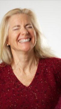 Vertical video of attractive mature woman listening to conversation with hand near ear, expressing doubts, unsure, suffering hearing problems at older age. Studio shot on white background