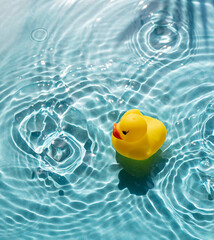 Bright yellow rubber duck floats in blue water pool. Hot summer resort vacation concept
