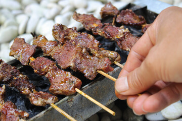 Close up of an asian man grilling beef satay on charcoal
