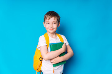 Boy with a yellow backpack and a book in his hands against a blue background.