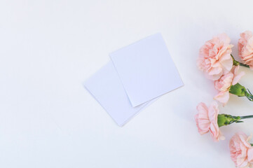 White sheets of stickers for notes lie on a white table with carnation flowers. Space for text
