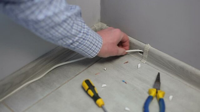 A male electrician lays a cable for television in the baseboard.