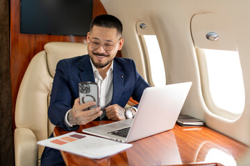 successful young asian businessman is sitting in private luxury jet with laptop and chatting via...