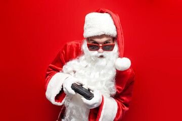 santa claus gamer in festive glasses and hat plays video game on gamepad on red background