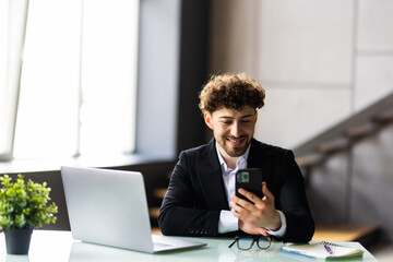 Obraz premium Young business man working at home with laptop and uses a smartphone in office