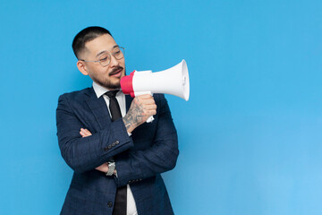 successful asian businessman in suit and glasses announces the news in megaphone on blue isolated...