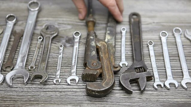 The man takes the largest wrench from the set of keys. Wrenches of different sizes on a wooden background.