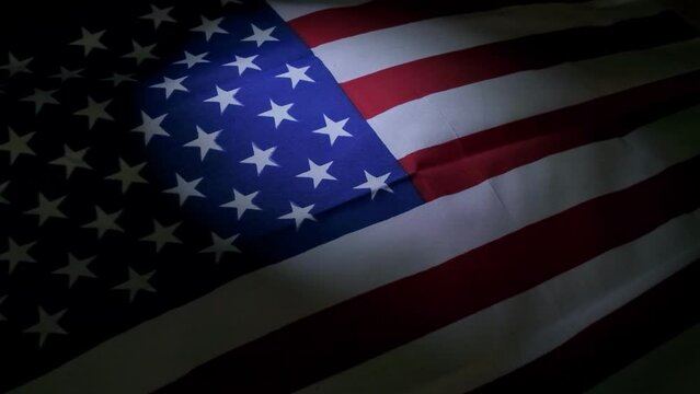 An intimate, slow-motion glimpse at the American flag, spotlight-illuminated against the darkness.