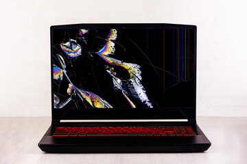 a gaming laptop with a broken screen in cracks on a gray background close up front view - 607867497