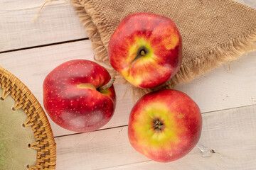 Three red apples with ceramic plate and jute napkin on wooden table, macro, top view.