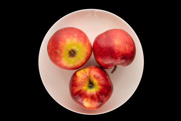 Three red apples in a ceramic plate on a black  background, macro, top view.