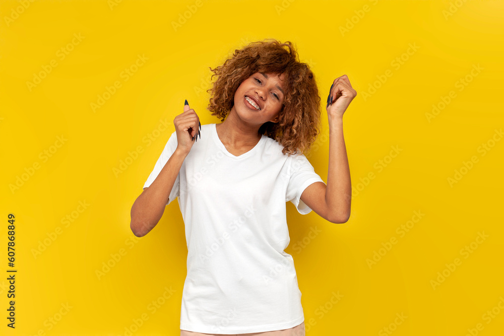 Wall mural young curly american girl dancing to the music on yellow isolated background