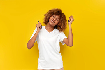 young curly american girl dancing to the music on yellow isolated background