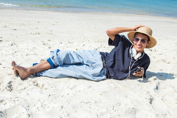 relaxed young man with headphones and mobile phone lying on the beach