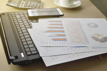Obraz premium graphs and charts. business reports and pile of documents with a coffee cup, glasses, smartphone, calculator place on desk.