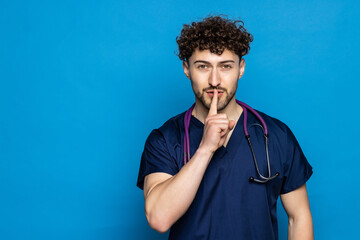 Fototapeta na wymiar Young doctor man with beard over blue background asking to be quiet with finger on lips. Silence and secret concept.