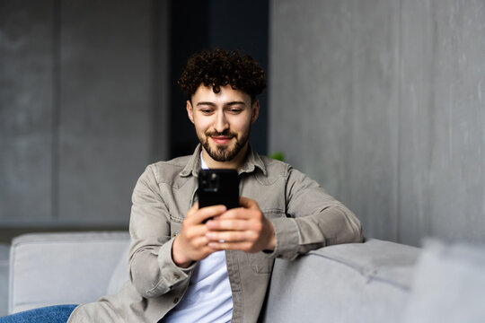 Content young man relax on sofa use smartphone spend free time online in social network chat at web app play easy game online.