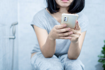 Asian woman using mobile phone sitting too long in the toilet can cause constipation and hemorrhoids