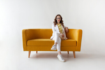 young businesswoman in suit sits and waits on comfortable soft sofa, girl in formal wear rests on yellow couch - Powered by Adobe