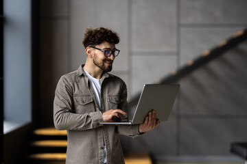 Portrait of handsome man office worker with laptop in hands standing in office