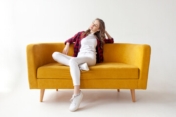 young cute girl sits on soft comfortable sofa and relaxes, pensive woman is resting on yellow couch
