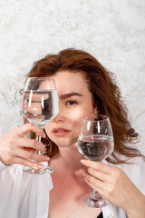 A beautiful healthy brunette girl is holding a glass of water or clear liquid, smiling happy positive. demonstrating product vitamins, hydrating drinks, alcohol.