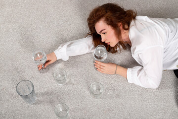 A beautiful healthy brunette girl is holding a glass of water or clear liquid, lying on a floor....