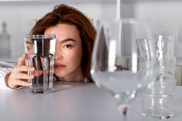 A girl is looking through a glass of water, visually distorting her face. emonstrating product vitamins, hydrating drinks, alcohol.