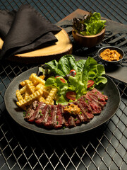 Medium rare sliced grilled meat steak Striploin with sauce, potato, salad on retro dish on metal net background.