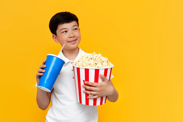 Asian little boy of ten years old with popcorn and soda is dreaming and looking at copy space