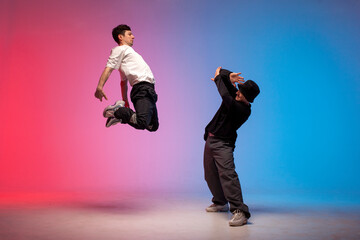two dancer guys break dance on red blue background and do trick together, male acrobats perform pair dance in neon