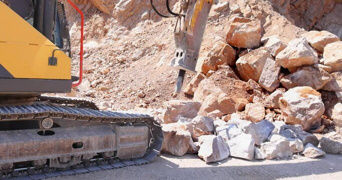 Excavator with hydraulic hammer breaking rock. Stone crushing machine at open pit mining and processing plant for crushed stone. Concepts of industry and building materials