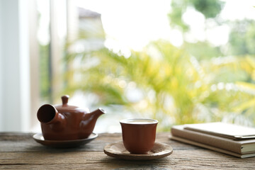 Earthenware teapot and tea cup and notebooks on wooden table