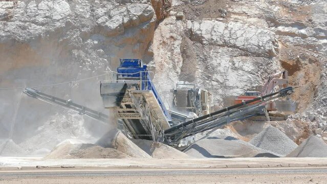 Stone crushing machine at open pit mining and processing plant for crushed stone. Piles of gravel stone and conveyor belts on the side of the road