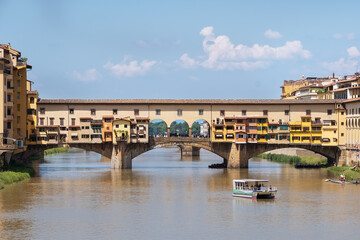 Fototapeta na wymiar Ponte Vecchio bridge over the Arno river with a touristic boat daytime photo in old Florence city, Toscana, Italy. Old architectural construction is unique and most visited attractive tourists sight.