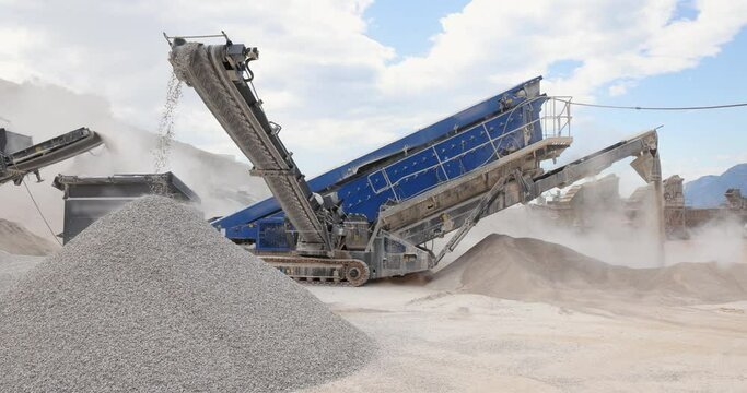 Stone crushing machine at open pit mining and processing plant for crushed stone. Piles of gravel stone and conveyor belts on the side of the road