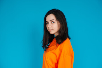 Fototapeta premium Stunning Young Woman in Trendy Orange Outfit Poses for Portrait, Isolated on Blue Background, Lovely Model with a Captivating Gaze and Gorgeous Appearance