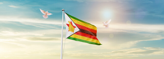 Waving Flag of Zimbabwe in Blue Sky. The symbol of the state on wavy cotton fabric.