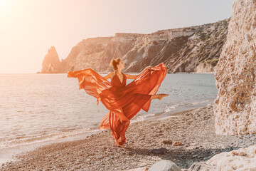 Woman red dress sea. Female dancer in a long red dress posing on a beach with rocks on sunny day. Girl on the nature on blue sky background.