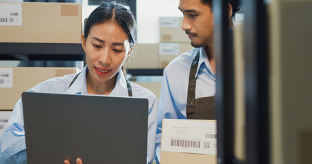 Asian business partner girl hold laptop and man wear formal shirt hold cardboard box training inventory online stock data program for delivery customer at warehouse. Startup small business concept.