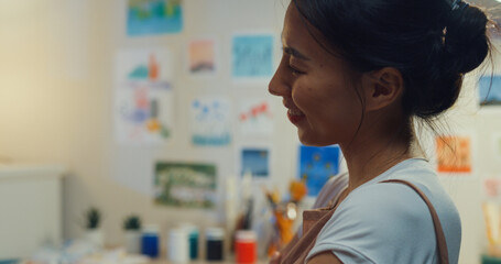 Youth Asia lady wear apron sit front of desk drawing picture on sketchbook create artwork cozy workshop in home at night. Contemporary Painter Abstract Modern Art, Creativity and people concept.