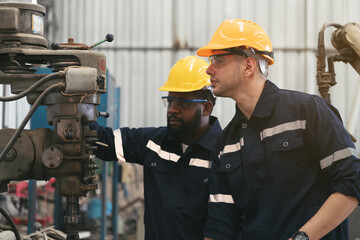 Two male engineer workers working with metal lathe machine at production line in factory, wearing safety uniform, helmet and protective gloves