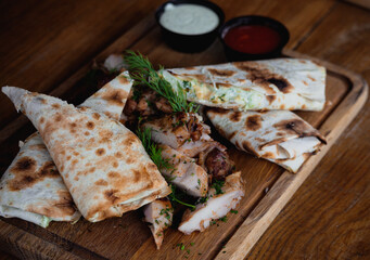 Shawarma chicken roll in a pita with fresh vegetables, cream sauce and french fries on wooden background. Selective focus