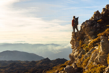 unrecognizable hiker with backpack and trekking poles standing on a rock contemplating the landscape at sunset. man on a mountain peak. sport & adventure
