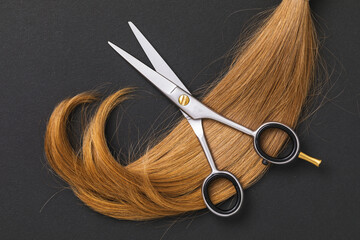 Scissors for cutting hair and a cut off strand of children's blond hair on a dark paper background