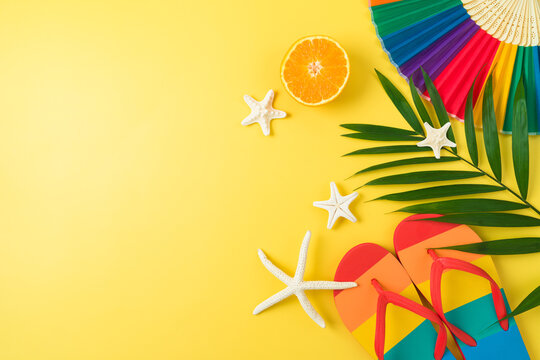 LGBTQ pride month beach party concept with rainbow flip flops palm leaf and  paper fan on yellow background. Top view, flat lay