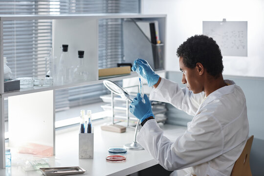 Side view portrait of ethnic young man doing tests at workstation in modern laboratory, copy space